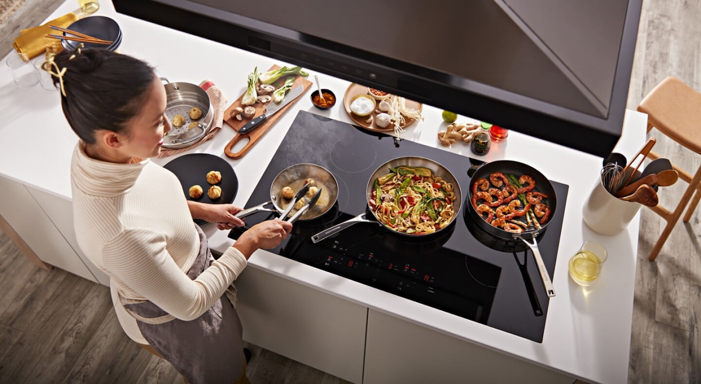 Bird's-eye view of person frying food on an electric stovetop beneath a range hood