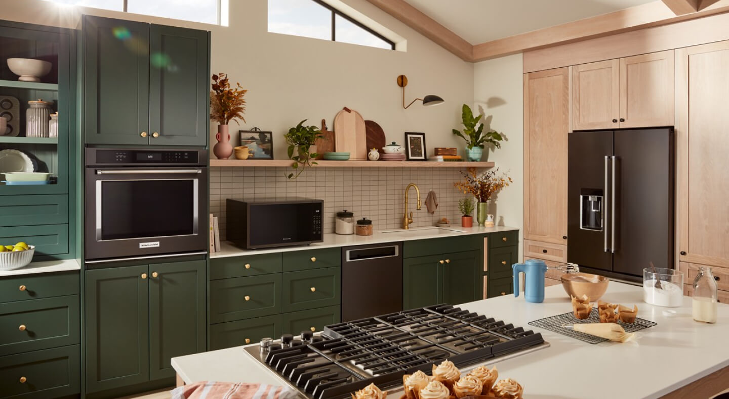 Suite of KitchenAid® black stainless steel appliances in dark green cabinetry