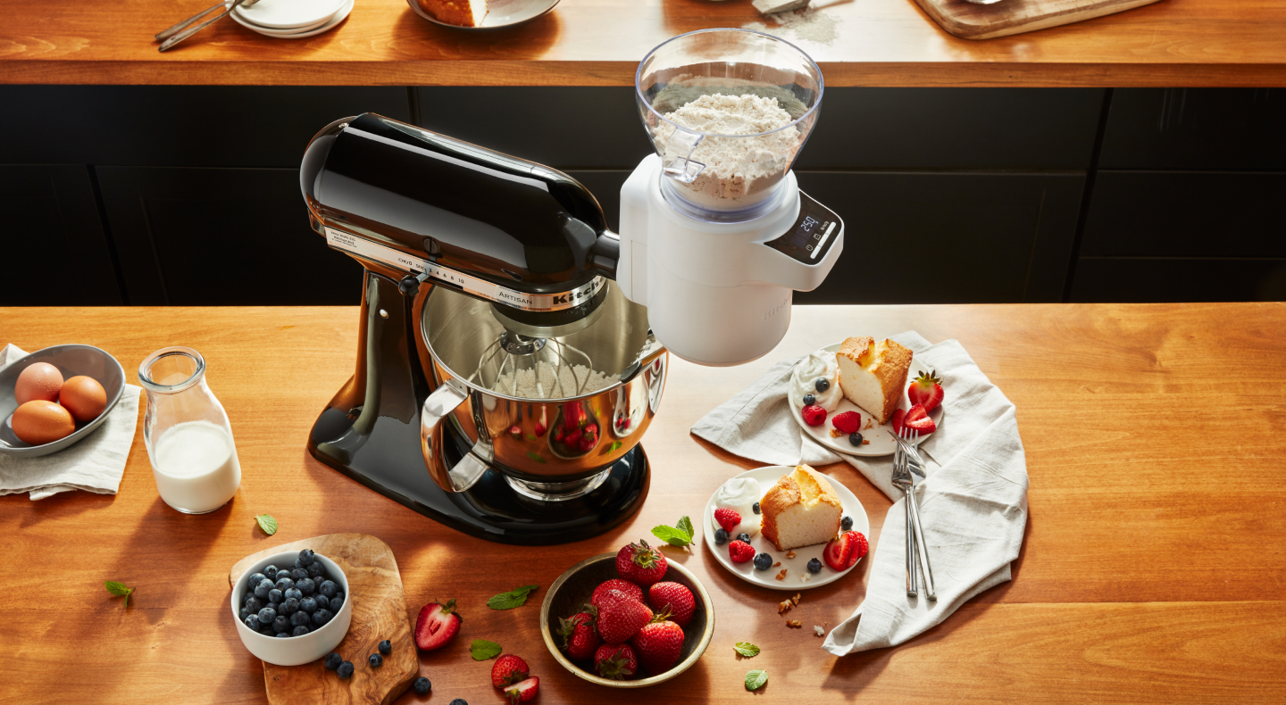 KitchenAid® Stand Mixer on wood countertop with fruits and cake nearby