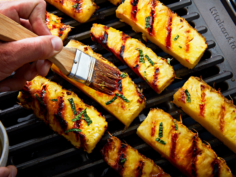 Hand dressing grilled pineapples with a pastry brush Hand dressing grilled pineapples with a pastry brush