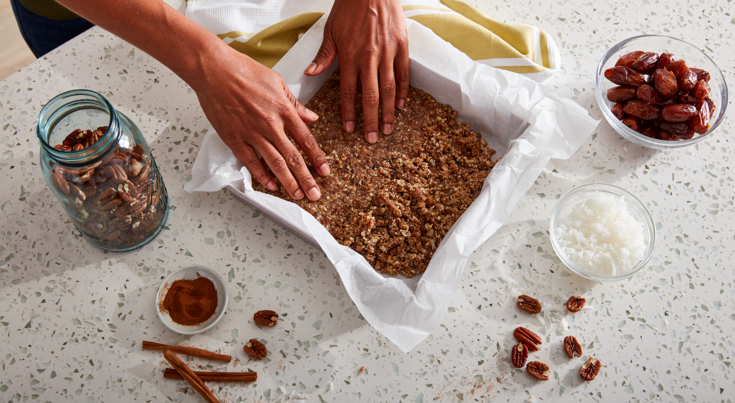 A pair of hands putting a baking dish together with ingredients consisting of coconut, dates, pecans and cinnamon A pair of hands putting a baking dish together with ingredients consisting of coconut, dates, pecans and cinnamon