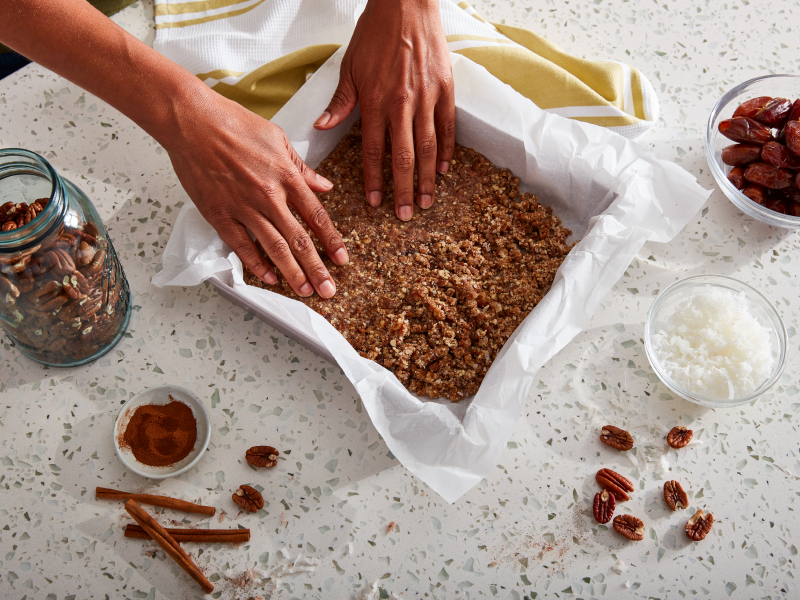 A pair of hands putting a baking dish together with ingredients consisting of coconut, dates, pecans and cinnamon A pair of hands putting a baking dish together with ingredients consisting of coconut, dates, pecans and cinnamon