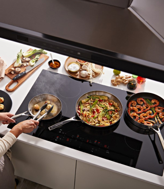 A person cooking vegetables and shrimp on cooktop