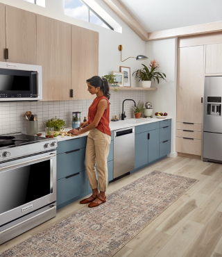 A person in an L-shaped kitchen with blue and brown cabinetry