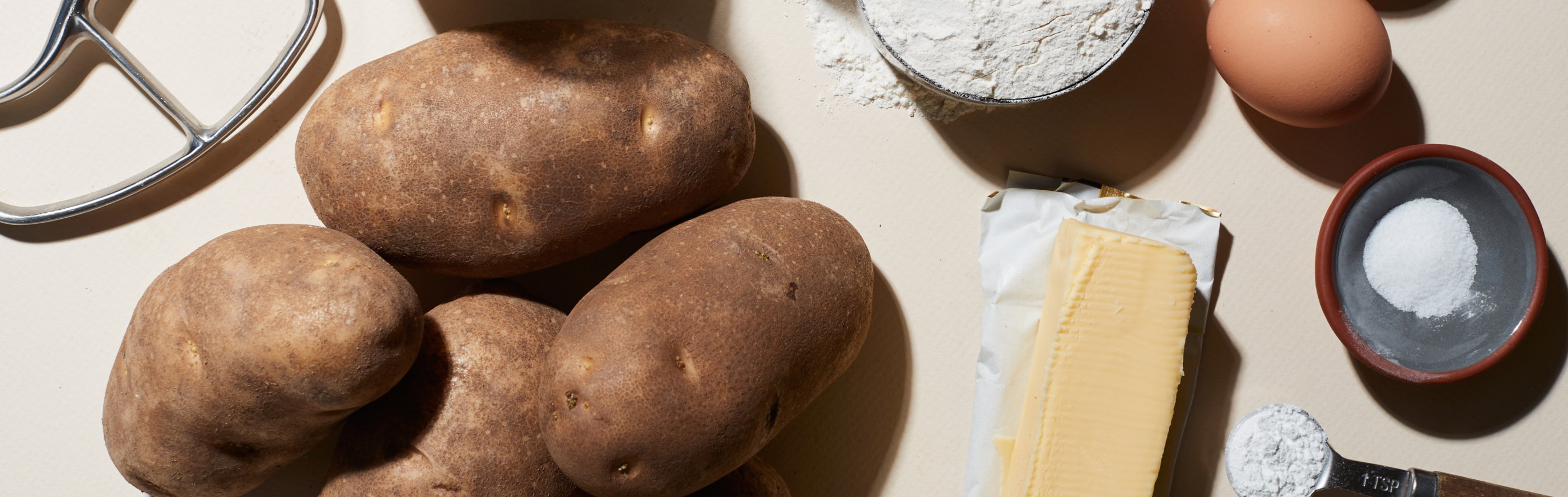 Russet potatoes on white countertop with assorted ingredients