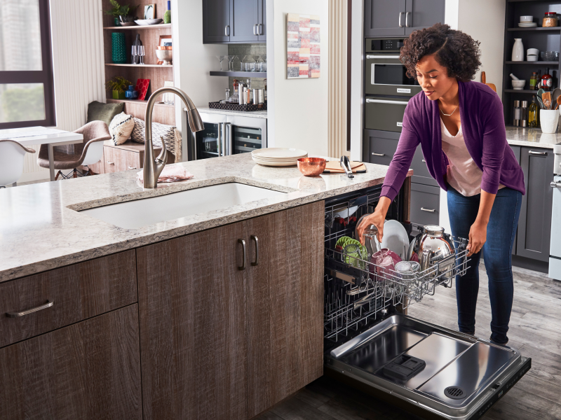 A woman loading a glass onto the top rack of an open dishwasher A woman loading a glass onto the top rack of an open dishwasher