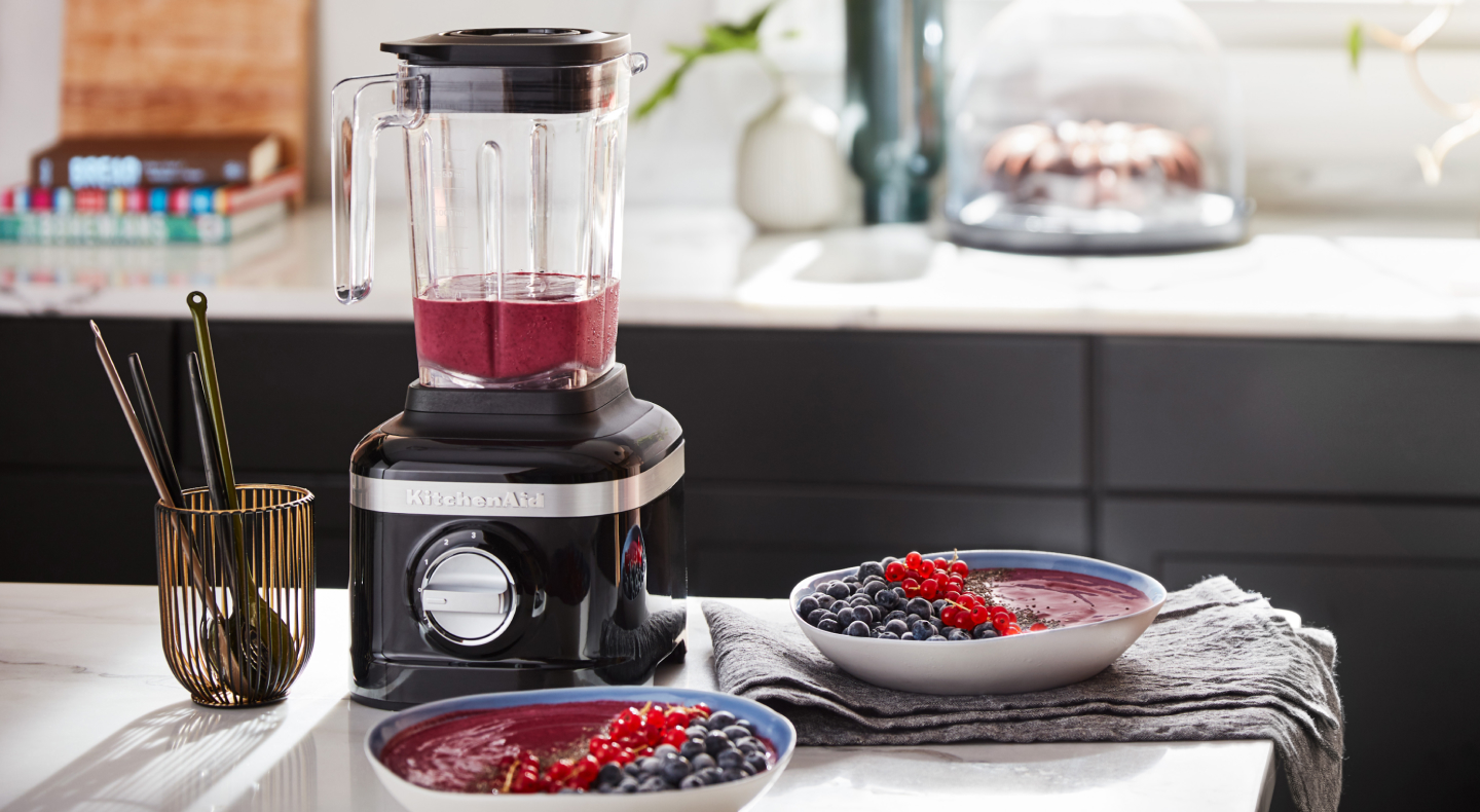 Black KitchenAid® blender next to two smoothie bowls garnished with fresh fruit
