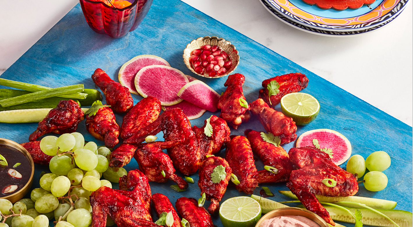 Hibiscus glazed wings on a serving board with different colored food accompanying the dish. 