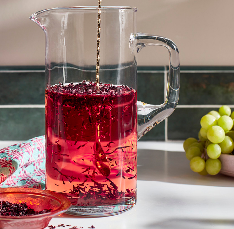 A cup of hibiscus tea, with hibiscus leaves scattered around the mug.