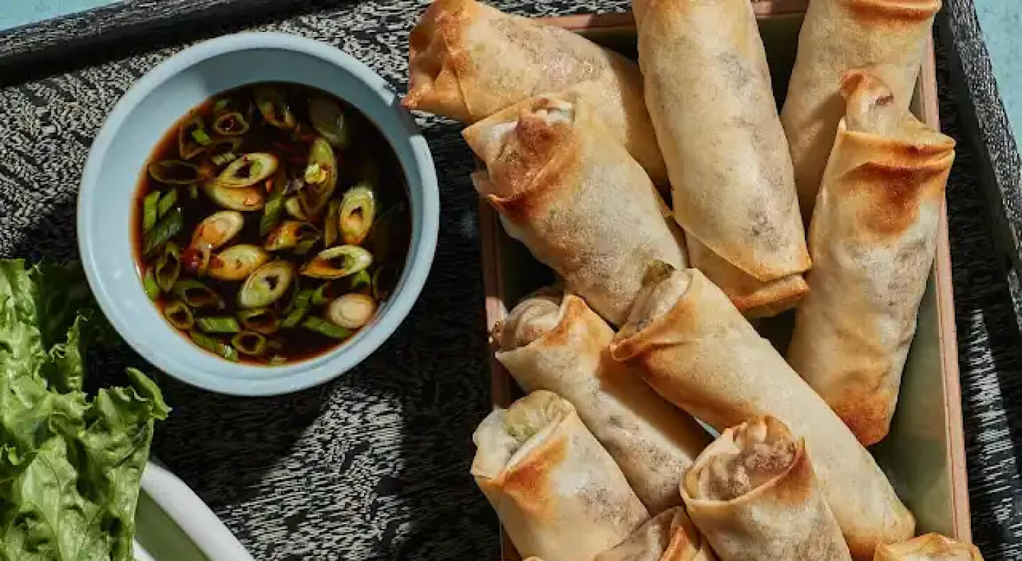 Pork and shrimp spring rolls on platter by dipping sauce