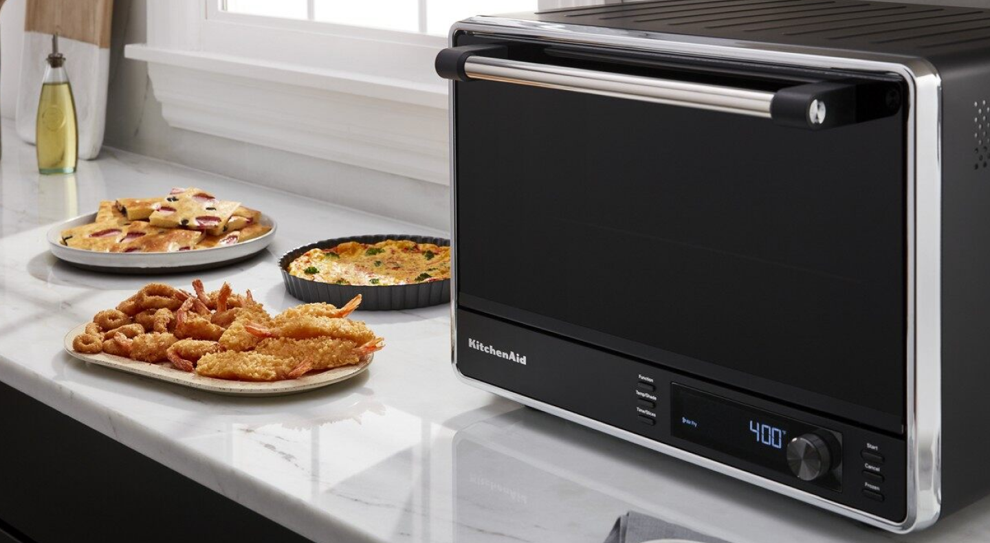 A KitchenAid® convection countertop oven next to plates of food A KitchenAid® convection countertop oven next to plates of food