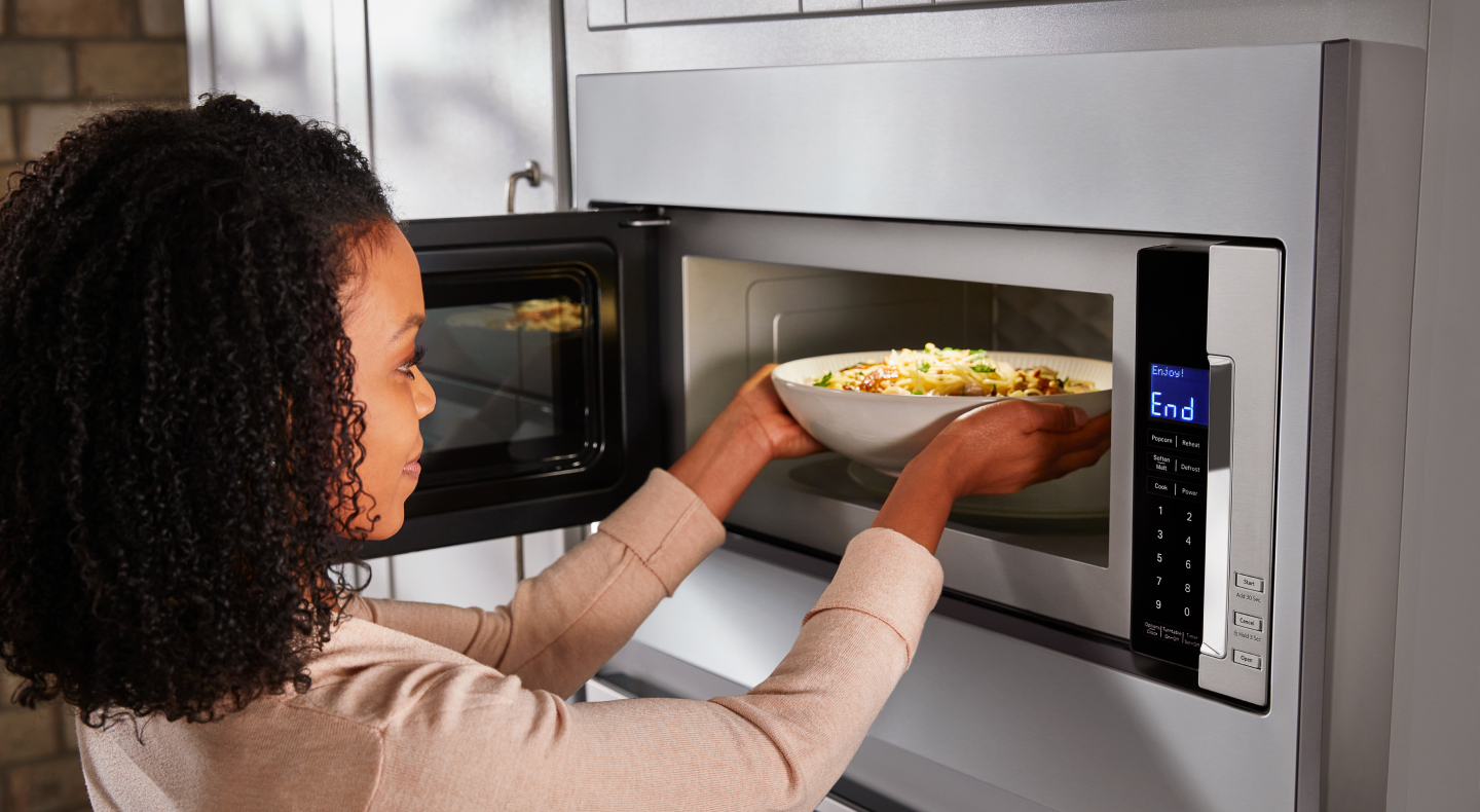 Woman placing a bowl inside built-in microwave Woman placing a bowl inside built-in microwave