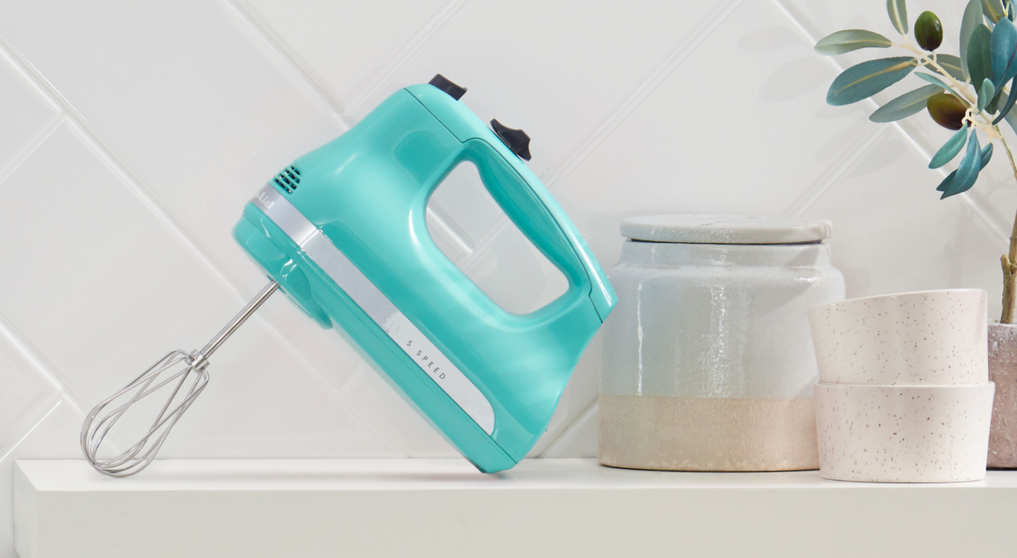 A teal KitchenAid® hand mixer on a modern kitchen counter. A teal KitchenAid® hand mixer on a modern kitchen counter.