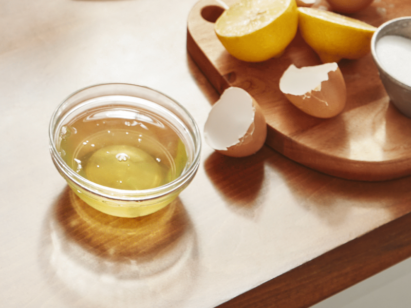 Egg whites in a bowl next to a cracked egg.