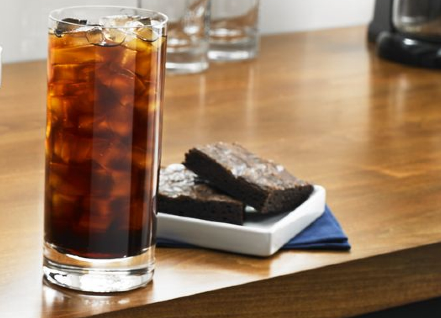 Tall glass of black iced coffee next to two brownies Tall glass of black iced coffee next to two brownies