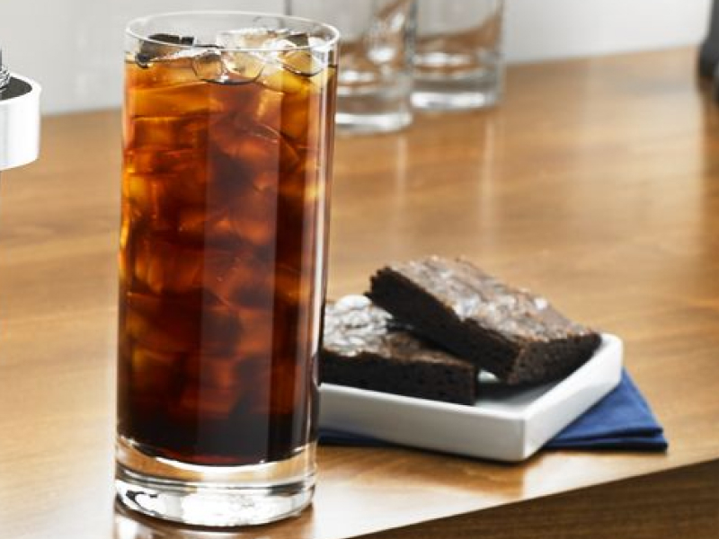 Tall glass of black iced coffee next to two brownies Tall glass of black iced coffee next to two brownies