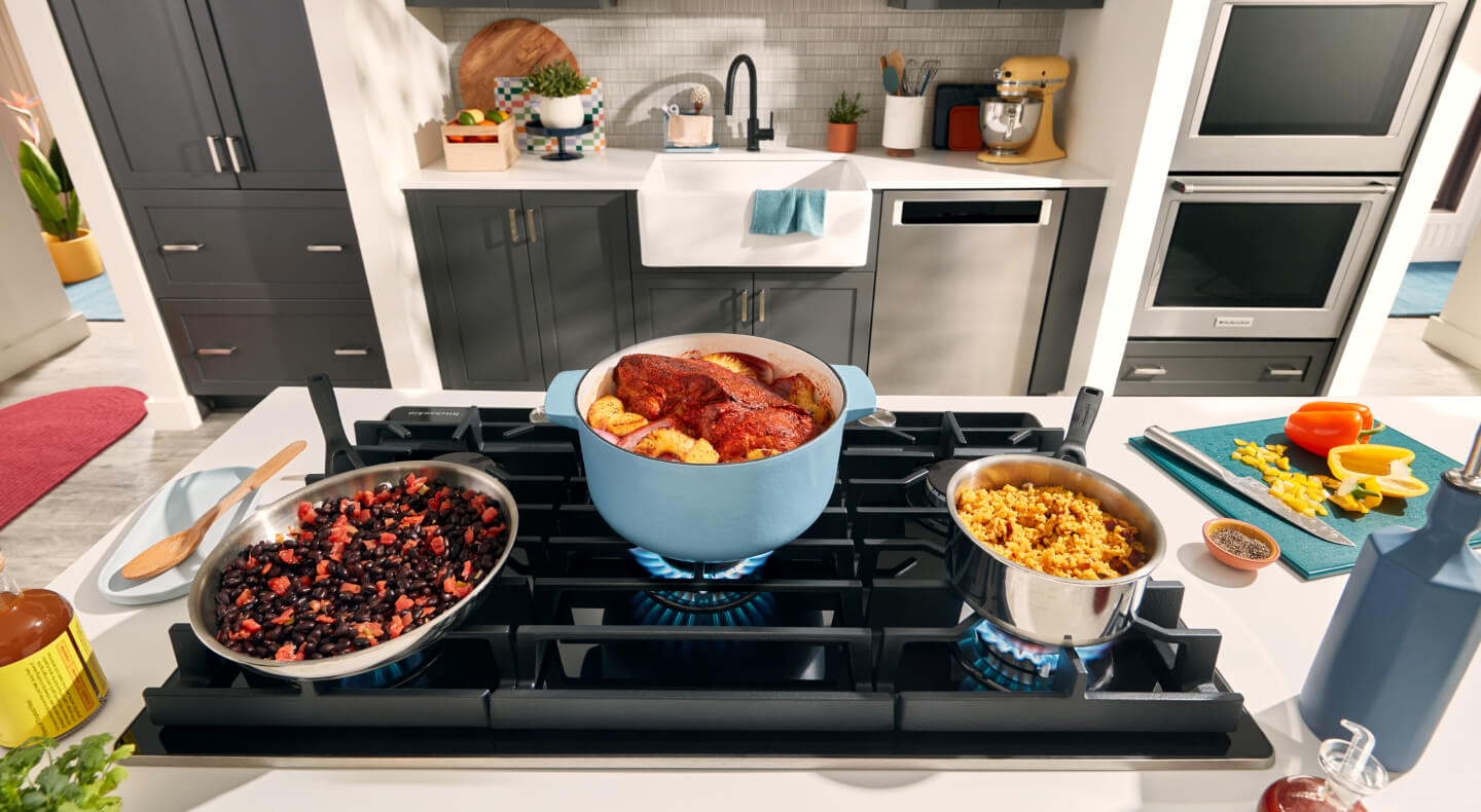 Dishes cooking in stock pots and a wok above the open flame of a gas cooktop