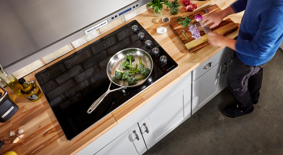 Broccoli resting in a pan and vegetables being sliced on a cutting board Broccoli resting in a pan and vegetables being sliced on a cutting board