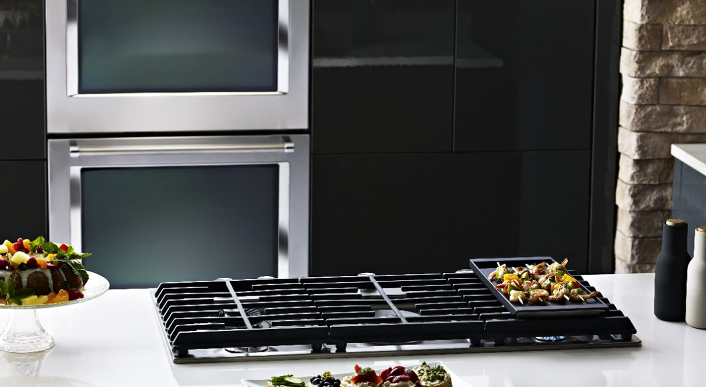 A KitchenAid® gas cooktop with a double KitchenAid® wall oven in the background A KitchenAid® gas cooktop with a double KitchenAid® wall oven in the background
