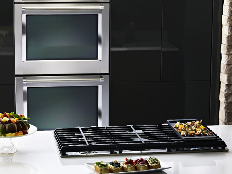 A KitchenAid® gas cooktop with a double KitchenAid® wall oven in the background A KitchenAid® gas cooktop with a double KitchenAid® wall oven in the background
