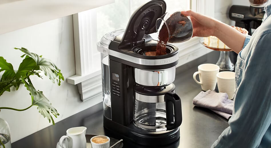 Person pouring coffee grounds into a KitchenAid® 12-Cup Coffee Maker Person pouring coffee grounds into a KitchenAid® 12-Cup Coffee Maker