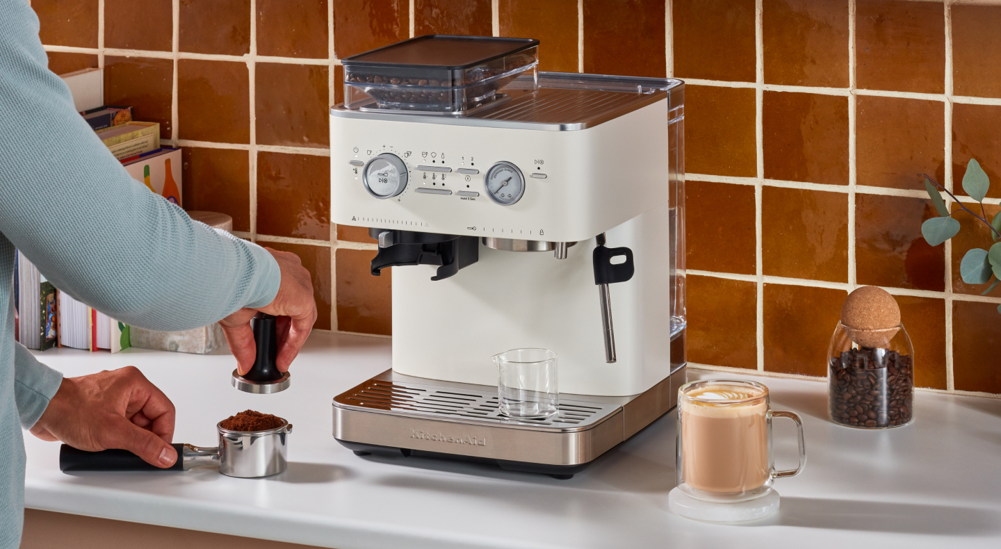 Person tamping espresso next to a KitchenAid® Semi-Automatic Espresso Machine