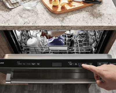 Top view of a slightly ajar front control panel dishwasher door with a loaded top rack