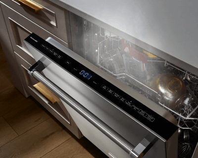 Top view of a slightly ajar front control panel dishwasher door with steam coming out