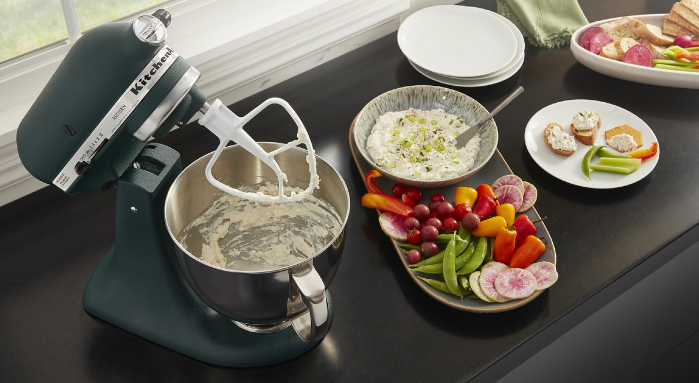 Black KitchenAid brand stand mixer with a flat beater making dip Black KitchenAid brand stand mixer with a flat beater making dip