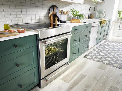 A long row of dark green cabinetry with stainless steel appliances, white countertops and white tile backsplash