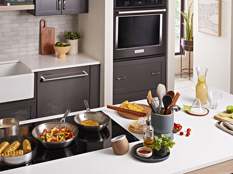 A galley kitchen with dark brown cabinetry, white countertops, a sink and built-in oven on one side, and an island with white countertops and a stovetop on the other A galley kitchen with dark brown cabinetry, white countertops, a sink and built-in oven on one side, and an island with white countertops and a stovetop on the other