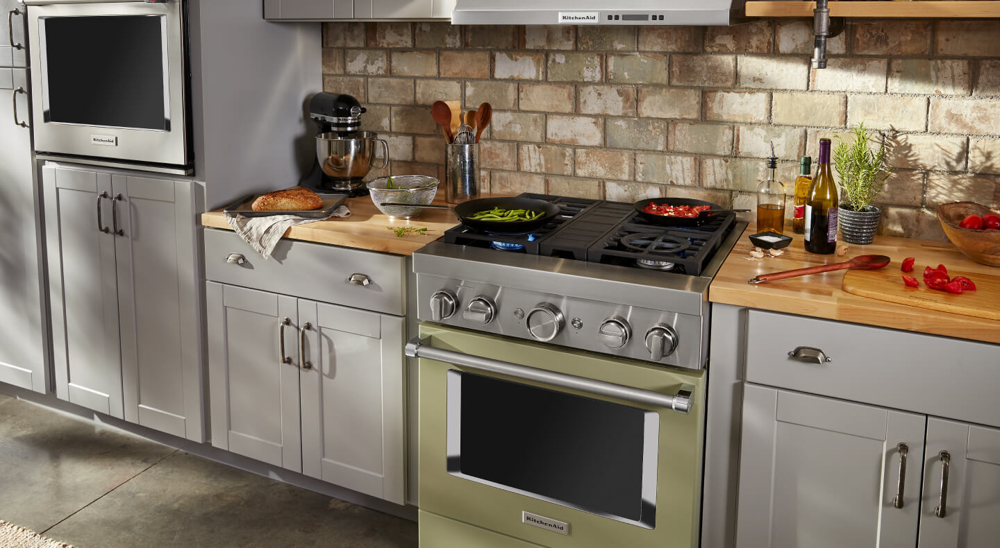 A KitchenAid® commercial style range set in gray cabinetry with a brick backsplash