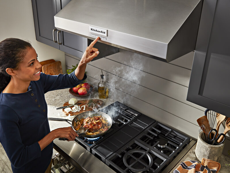 Person cooking on a gas range and selecting an option on the range hood