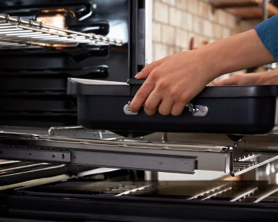 Person removing a baking dish from a wall oven slide-out rack