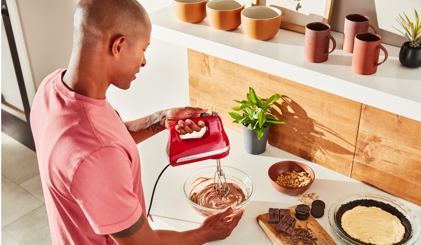 A man using a KitchenAid® hand mixer to make chocolate pie filling. A man using a KitchenAid® hand mixer to make chocolate pie filling.