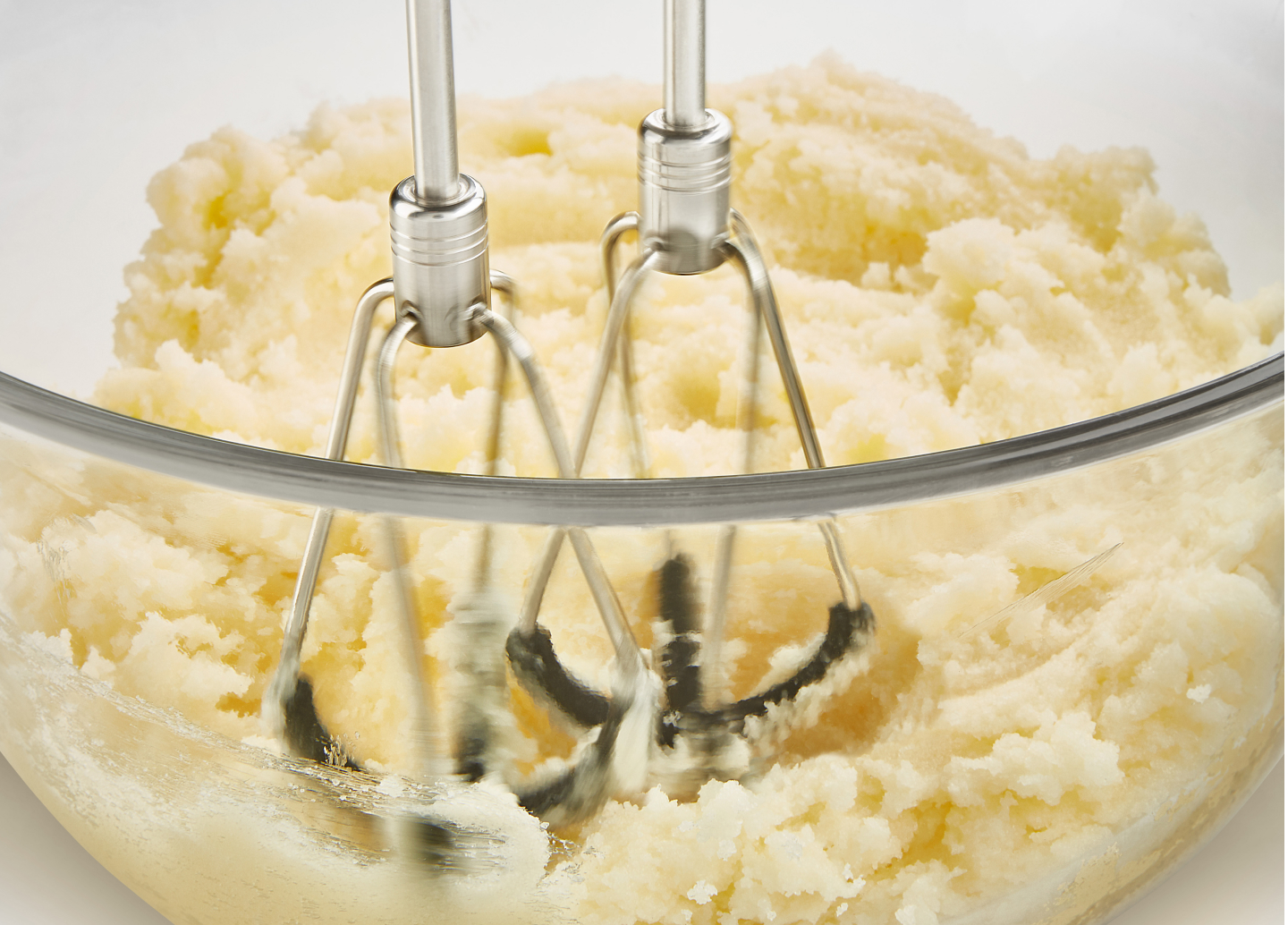 A closeup of KitchenAid® hand mixer beaters mashing potatoes. A closeup of KitchenAid® hand mixer beaters mashing potatoes.