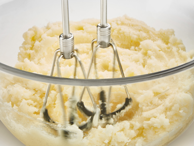 A closeup of KitchenAid® hand mixer beaters mashing potatoes. A closeup of KitchenAid® hand mixer beaters mashing potatoes.