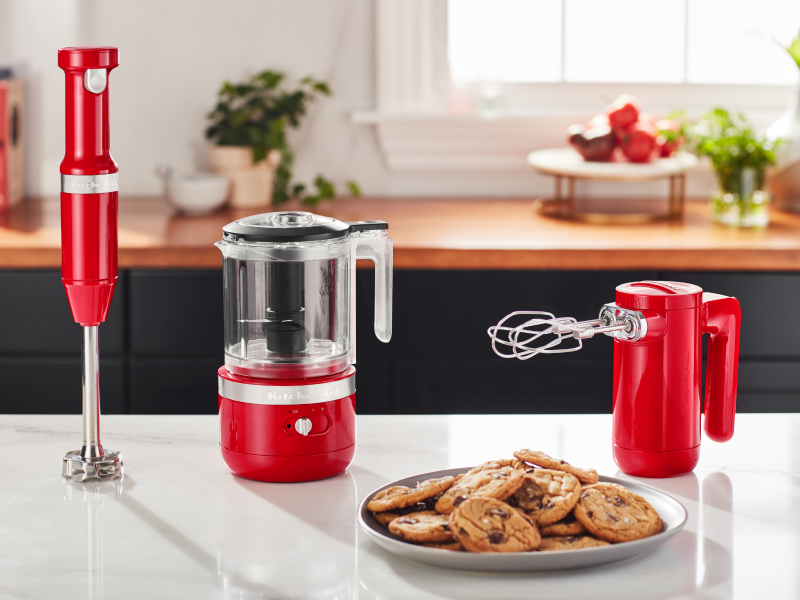 Cordless KitchenAid® hand mixer, hand blender and food chopper next to a plate of freshly baked chocolate chip cookies. tbaCordless KitchenAid® hand mixer, hand blender and food chopper next to a plate of freshly baked chocolate chip cookies.