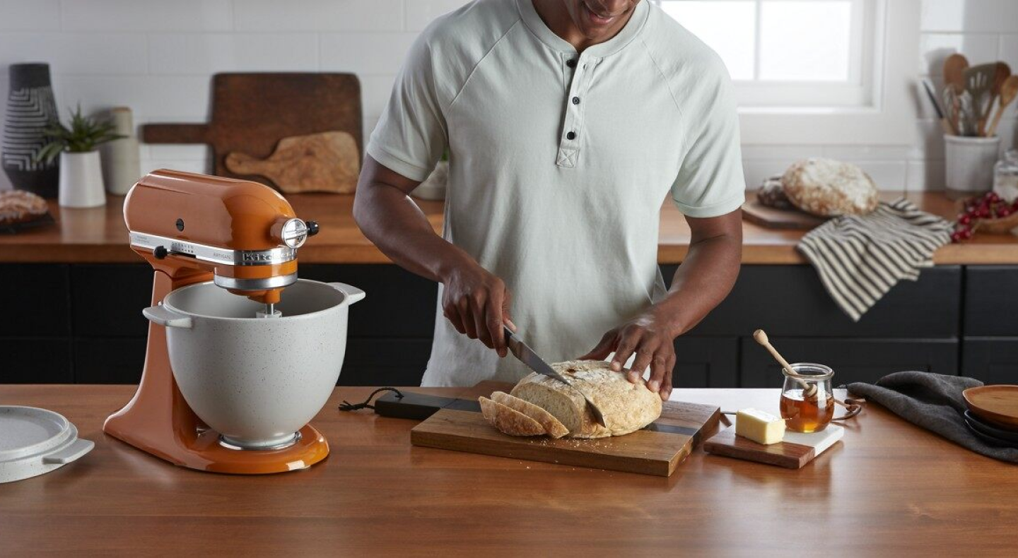 Person slicing bread next to a KitchenAid® stand mixer