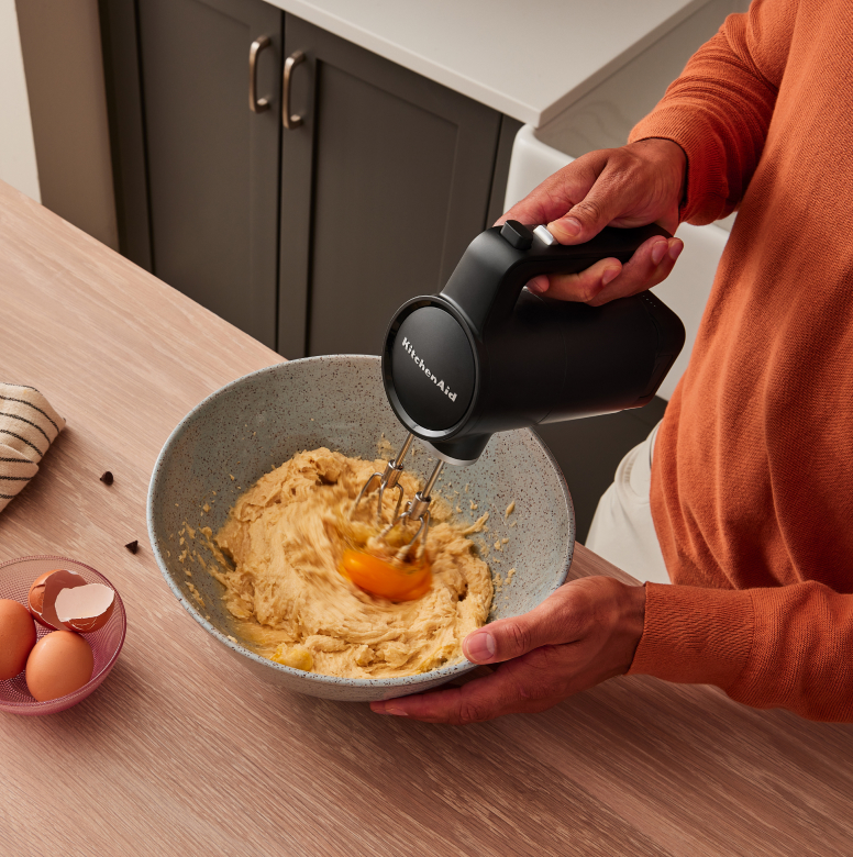 A person using a KitchenAid Go™ Hand Mixer to mix in eggs to batter.