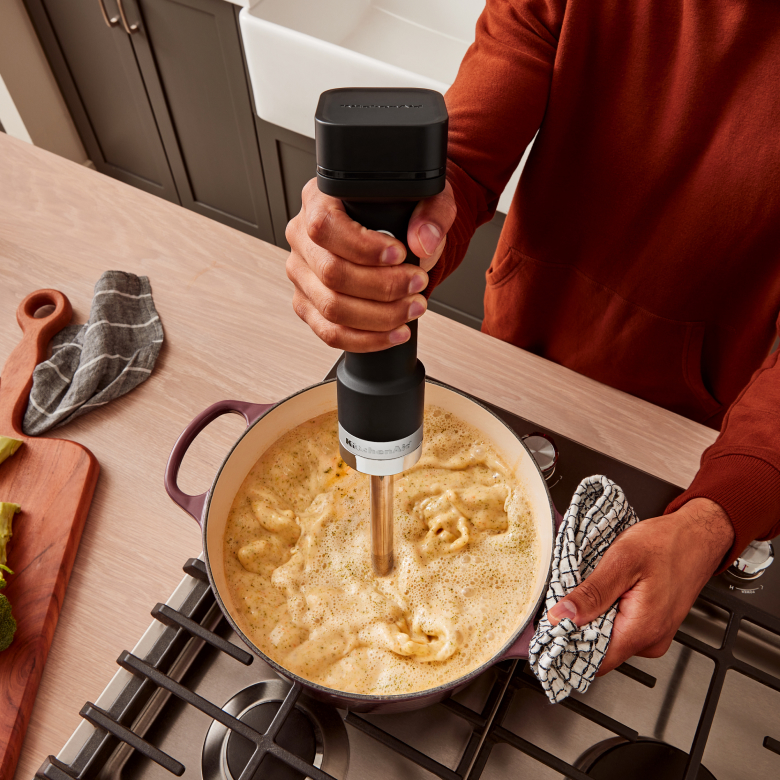 A person using a KitchenAid Go™ Cordless Immersion Blender in a pot of soup.
