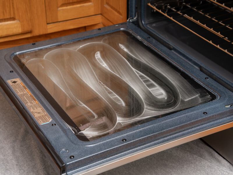 Oven door glass from the inside with a cleaning mixture spread all over it Oven door glass from the inside with a cleaning mixture spread all over it