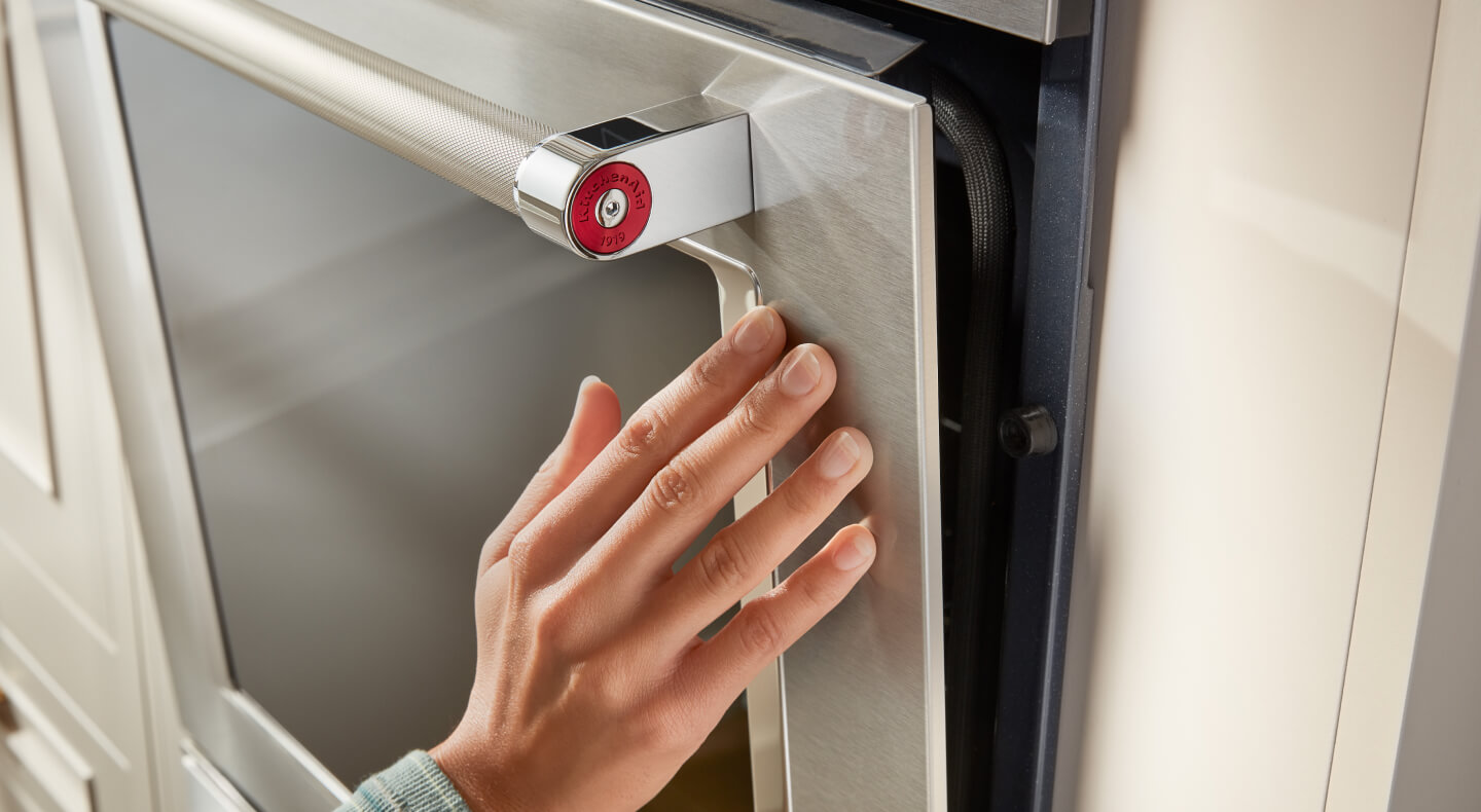 A hand touching a stainless steel oven door with a glass window in it A hand touching a stainless steel oven door with a glass window in it
