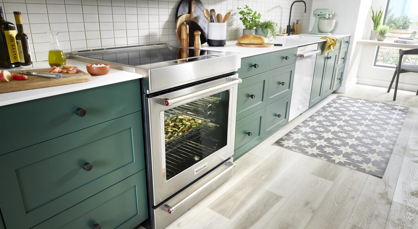 A  KitchenAid® range with vegetables cooking inside set into a countertop with green wooden details