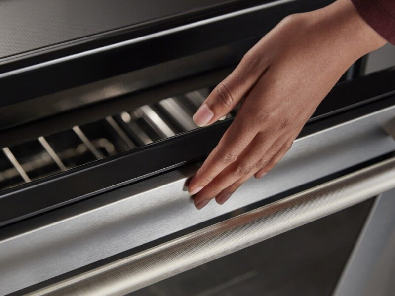 A person lightly touching an oven; the oven door glass is visible just below the person’s hand A person lightly touching an oven; the oven door glass is visible just below the person’s hand