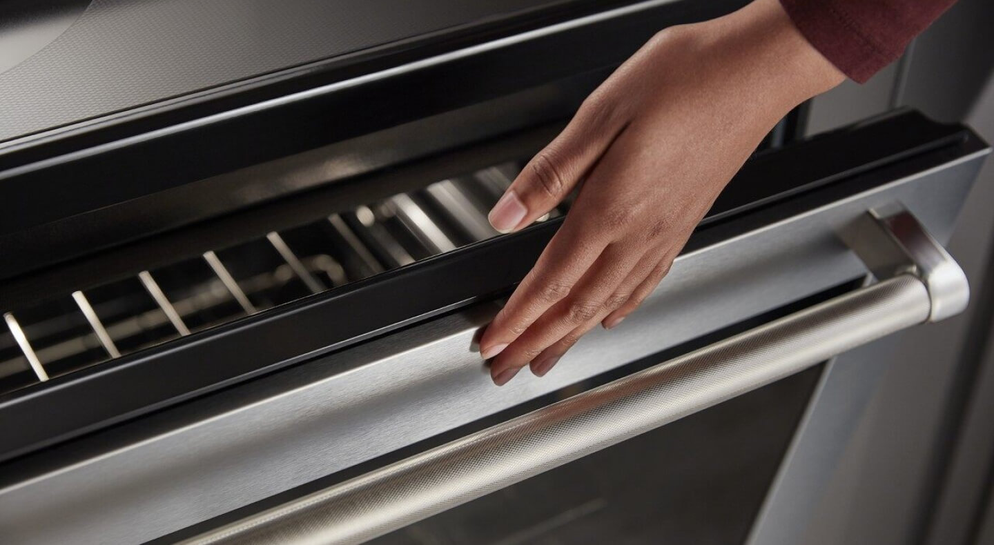 A person lightly touching an oven; the oven door glass is visible just below the person’s hand A person lightly touching an oven; the oven door glass is visible just below the person’s hand