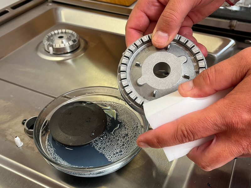 Hands shown gently cleaning a burner base on a gas stovetop