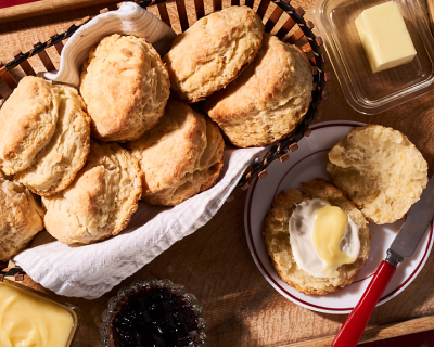 Basket of biscuits next to prepared biscuit on plate with butter knife Basket of biscuits next to prepared biscuit on plate with butter knife