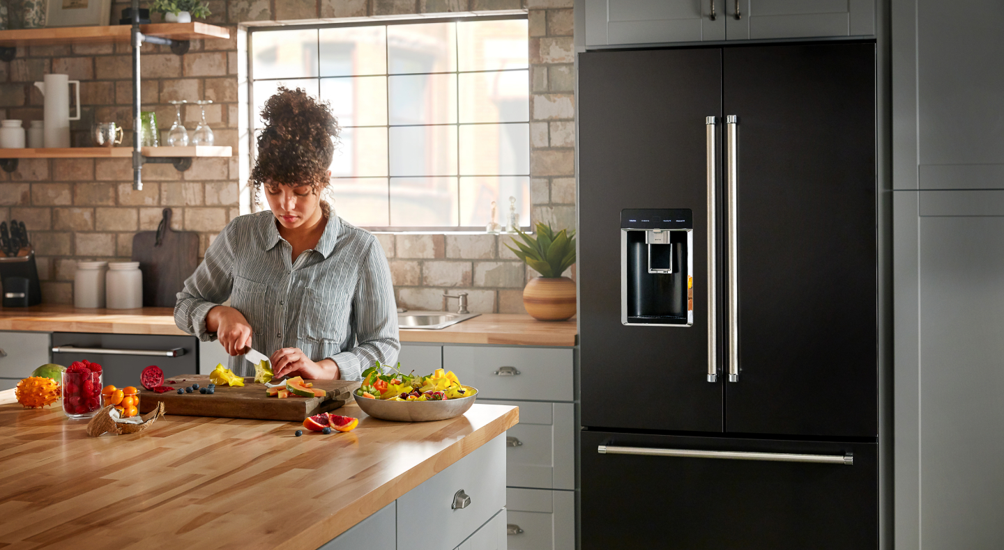A person making a meal in a modern kitchen next to a KitchenAid® refrigerator. A person making a meal in a modern kitchen next to a KitchenAid® refrigerator.