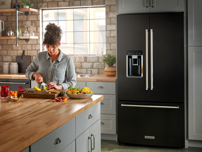 A person making a meal in a modern kitchen next to a KitchenAid® refrigerator. A person making a meal in a modern kitchen next to a KitchenAid® refrigerator.